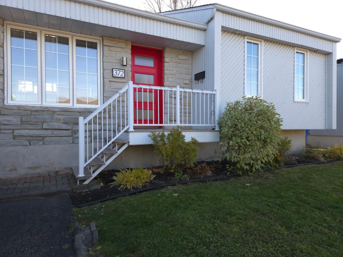 Façade du bungalow avec sa porte rouge distinctive et son revêtement de pierre